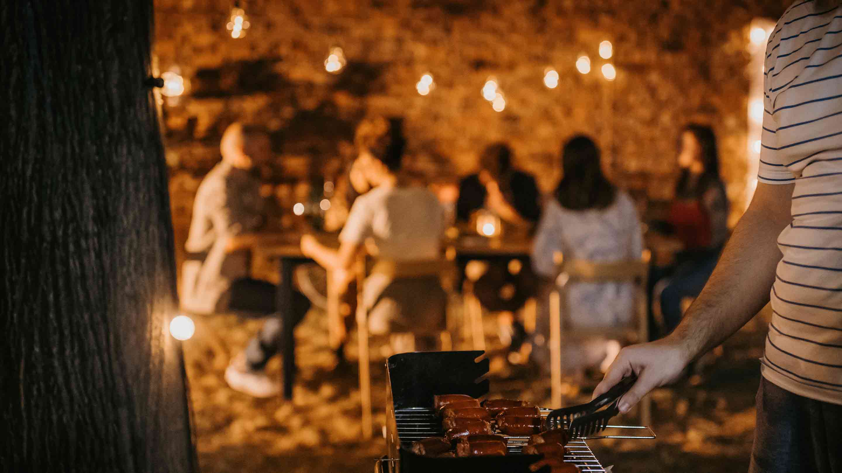 Приятели се наслаждават на барбекю вечер сред декорация от светлинки.