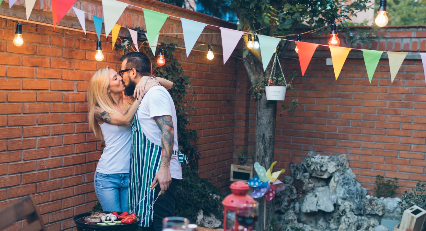 Двойка се целува, докато приготвя храна на грил.