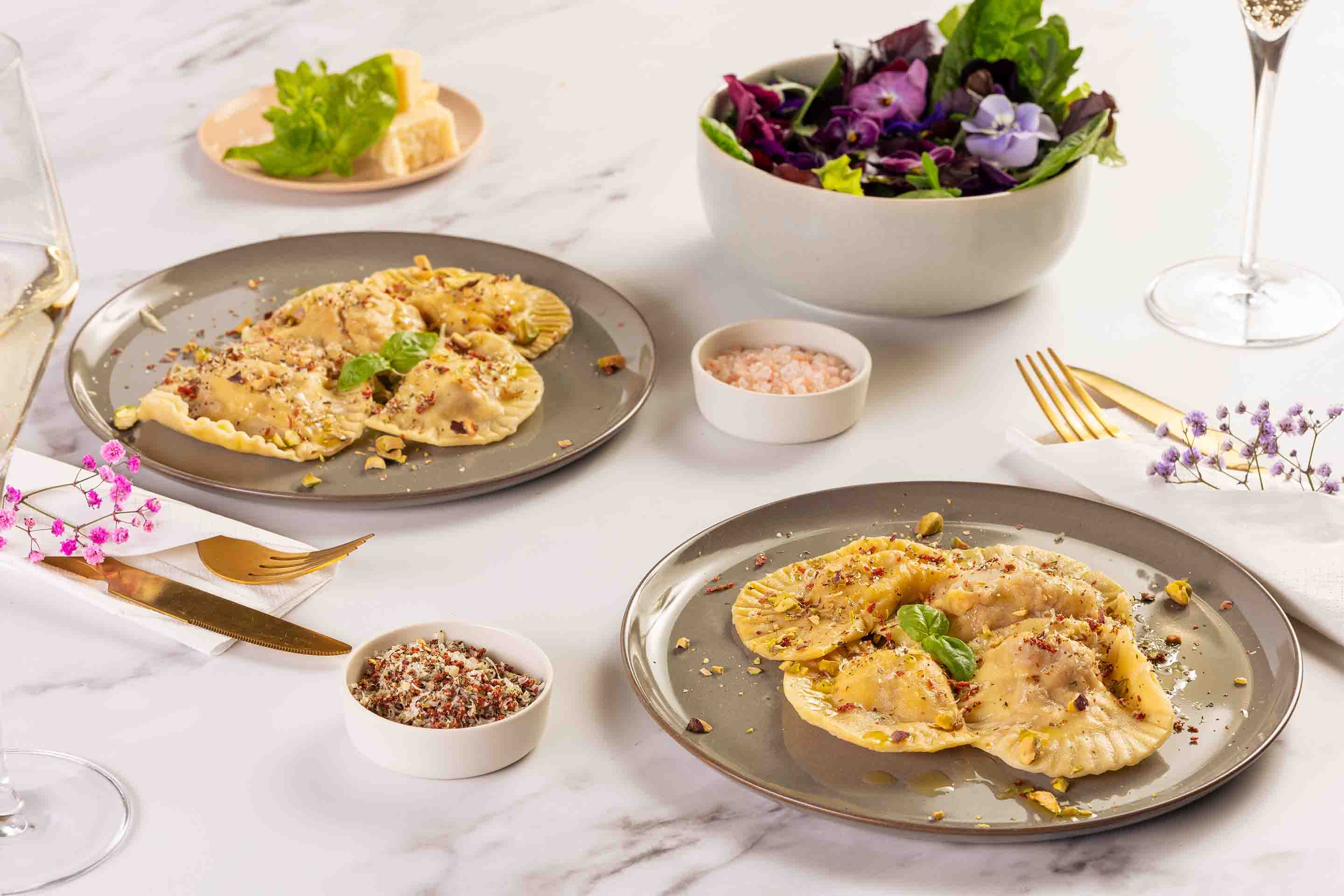 Две порции равиоли със сирене и орехи, поднесени с купичка зелена салата и златисти прибори.