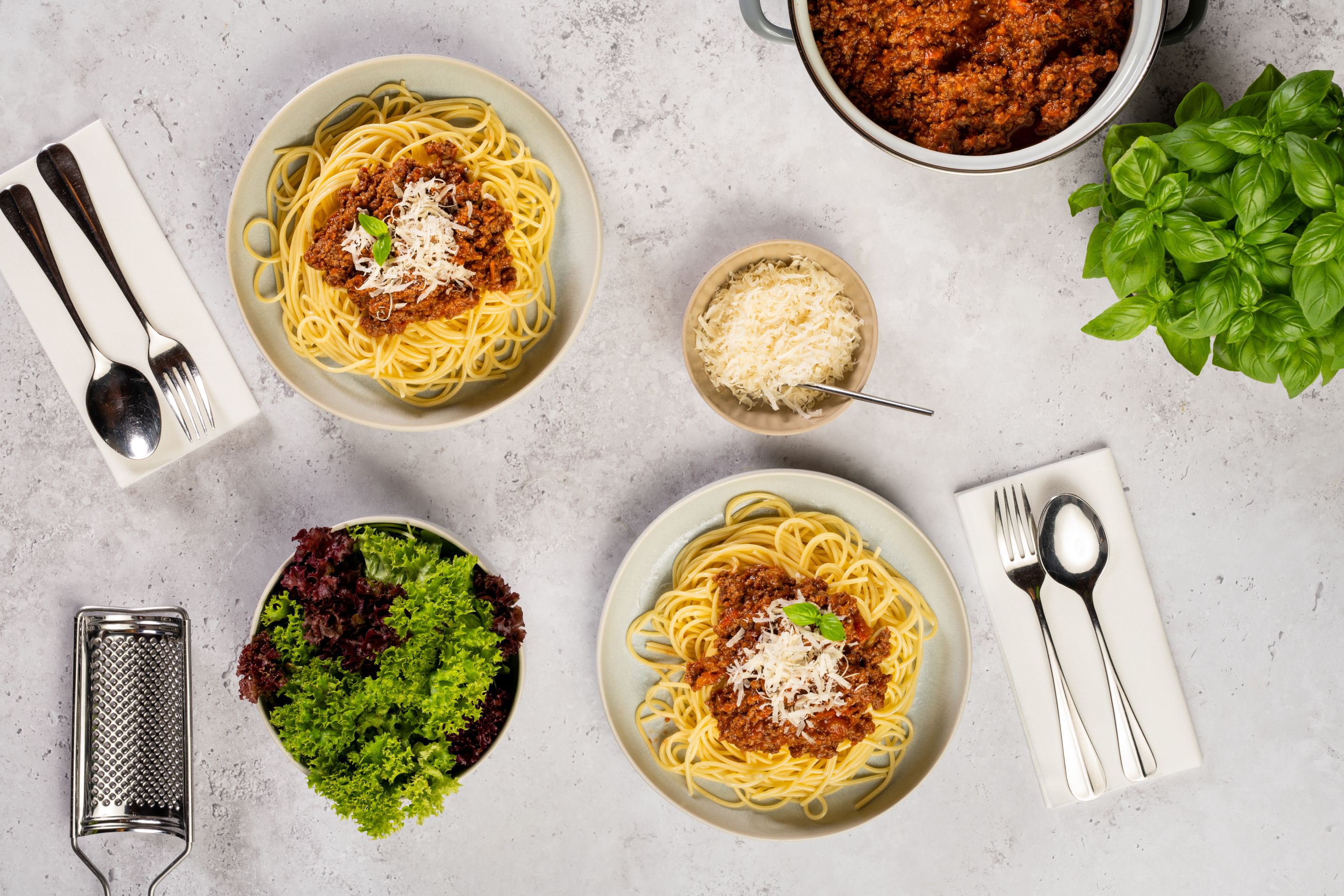 Спагети Болонезе с пармезан и листенца босилек, поднесени със зелена салата, допълнително пармезан и босилек.