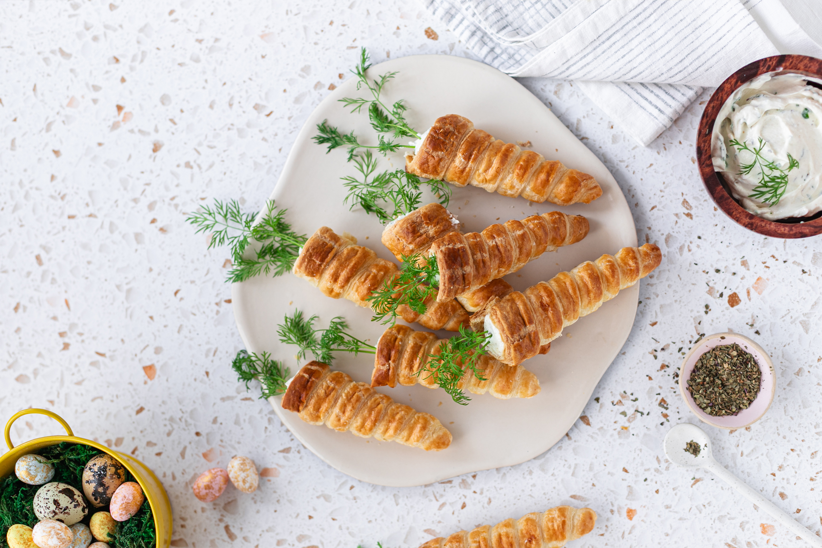 Чиния с порция от седем закуски от бутер тесто във формата на морковчета, с пълнеж и по стръкче копър забодено във всяко "морковче".